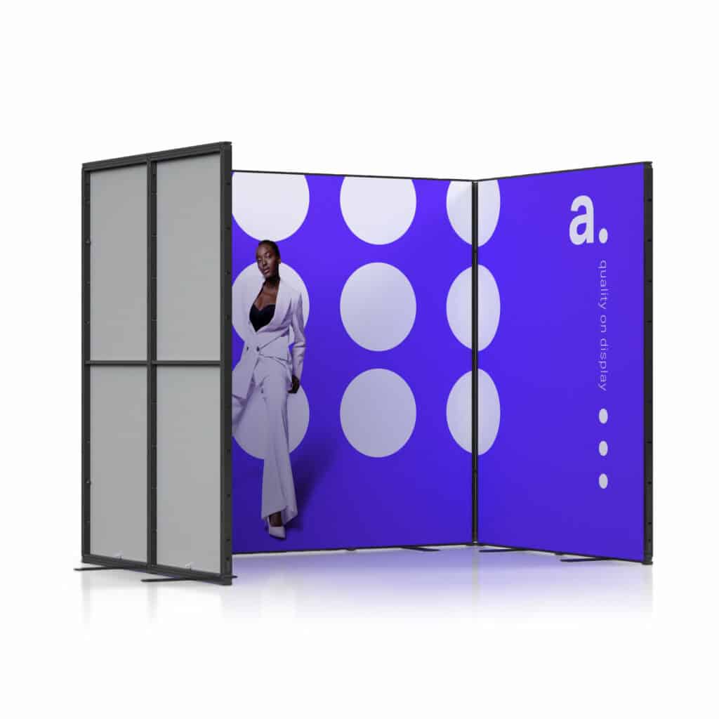 Beursstand Een moderne display met paarse panelen met grote witte stippen en een witte letter a. Een persoon in een wit pak poseert stijlvol op één paneel. De achterkant van de stand is effen grijs.