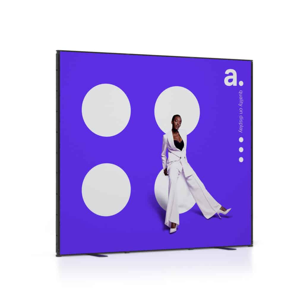 Beursstand Een vrouw in een stijlvol wit pak poseert tegen een paarse achtergrond met grote witte cirkels en de letter a. in de rechterbovenhoek. De woorden Affinity On Display verschijnen verticaal langs de rechterrand.