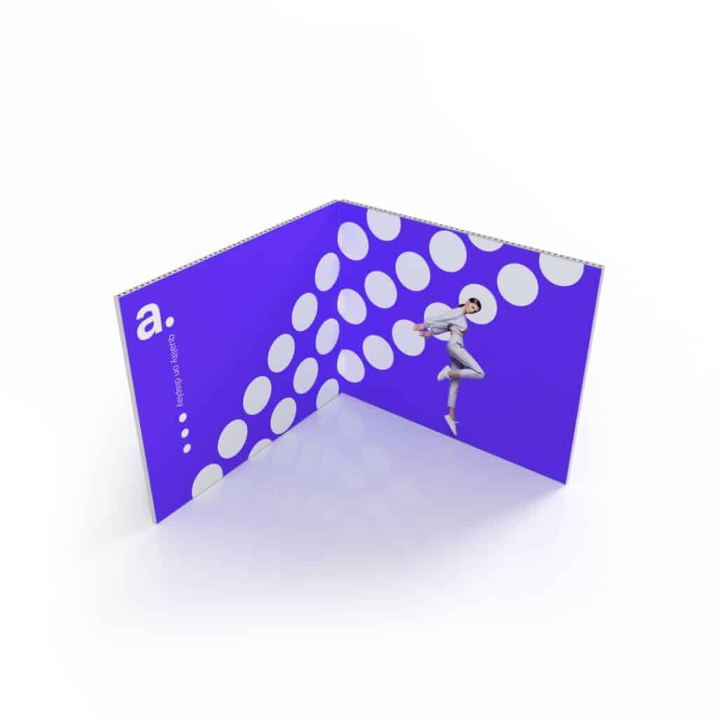 Beursstand Het Multiframe 3 x 3 meter - Hoekopstelling is een vrijstaand, V-vormig scherm met een felpaarse achtergrond met witte stippen, een kleine letter 'a' aan de ene kant en een atletisch springend persoon aan de andere kant.