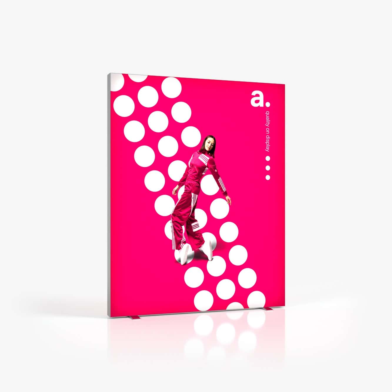 Beursstand Een vrouw in een felroze trainingspak springt voor de Portable LED LMD - 200x200cm (kopie) achtergrond met opvallende witte stippen, een magenta achtergrond en de letter "a." in de rechterbovenhoek tegen een strakke, minimalistische witte vloer en muur.