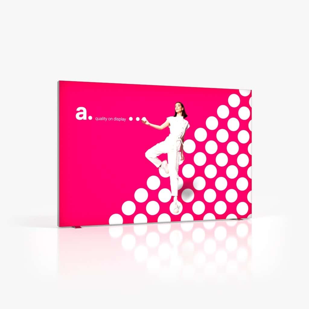 Beursstand Een vrouw in het wit poseert voor een levendige roze achtergrond met grote witte stippen, waarop de Portable LED LMD - 300x200cm wordt getoond. De moderne, minimale setting heeft naast haar de tekst "a. quality on display".