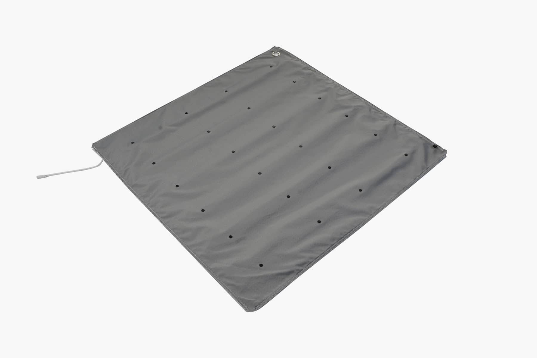 Beursstand De Portable LED balie - Expo 100x100cm is een grijze, vierkante stoffen mat met gelijkmatig verspreide kleine gaten en een hoekdoorvoer met lus, plat neergelegd op een witte achtergrond.